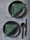 Four-piece cloth napkin set featuring a celestial print of radiant golden crescent moons and pale sunburst orbs against a rich emerald green background. Each napkin displays symmetrical, glowing motifs inspired by lunar phases and cosmic geometry. The fabric is neatly folded to showcase the repeating pattern, with a soft matte finish and fine detailing, perfect for mystical or magical table settings, altar decor, or celestial-inspired dining aesthetics.